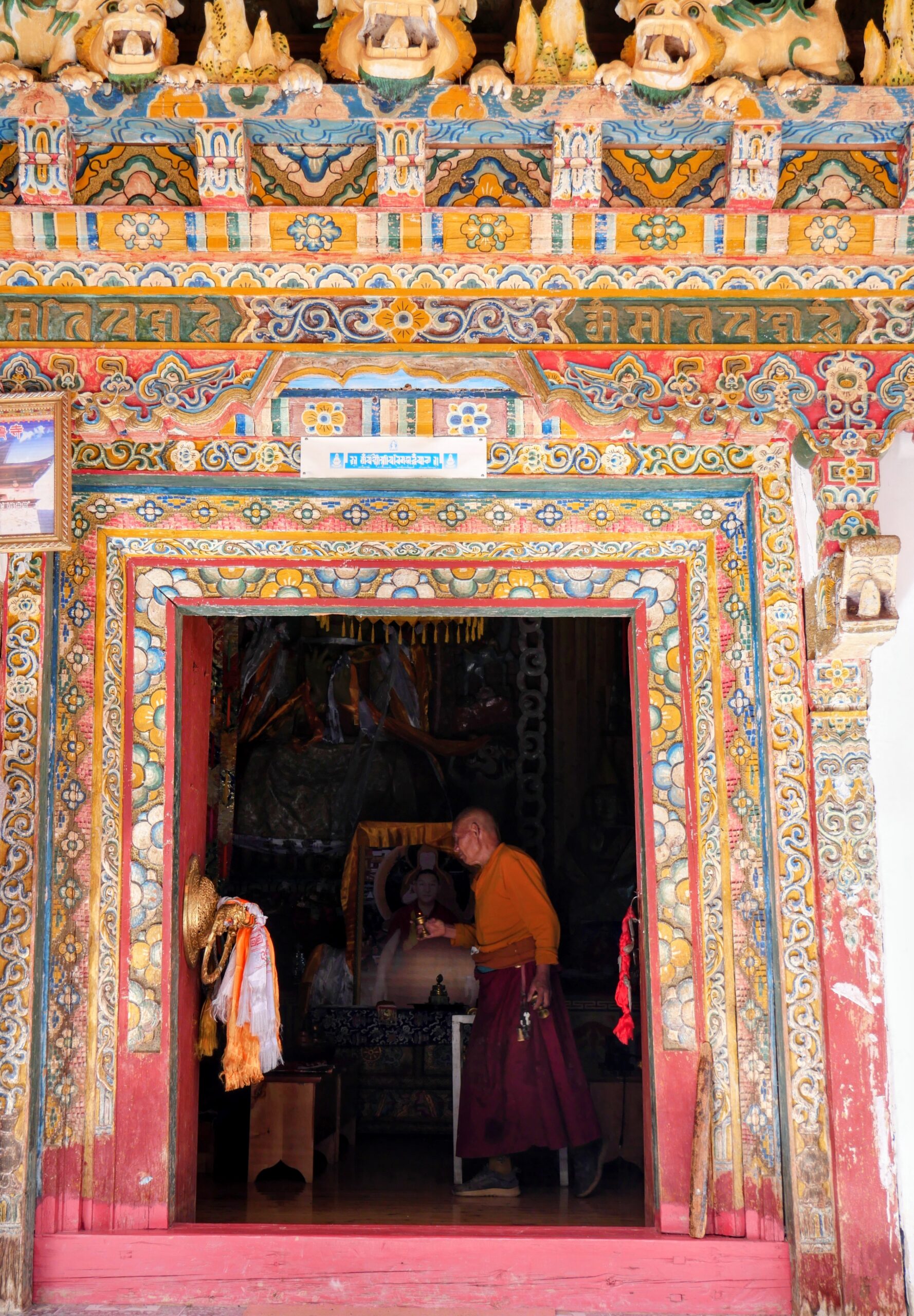 Ein buddhistischer Mönch im orangefarbenen Gewand betritt ein prachtvoll verziertes Tempelportal in Xialuo.